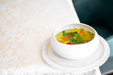 Bowl of homemade vegetable soup with tomatoes, carrots, and herbs on a white plate atop a floral...