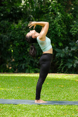 Peaceful full shot of a woman in an upward salute pose, practicing yoga in a lush green environment. A woman performs a graceful yoga pose outdoors, showcasing flexibility and wellness in nature.