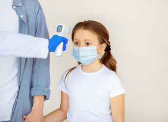 Doctor checking little girl's temperature with infrared thermometer before coronavirus vaccination...