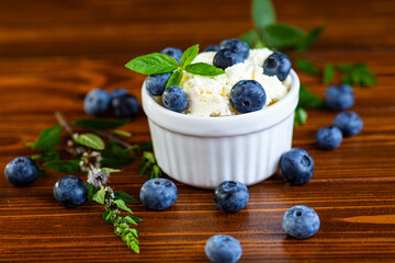 A bowl of cottage cheese decorated with blueberries and leaves on a wooden table