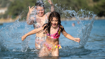 Fototapeta premium The sisters having fun together playing and splashing water in the sea during vacation