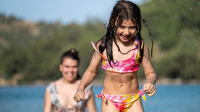 The sisters having fun together playing and splashing water in the sea during vacation - Powered by Adobe