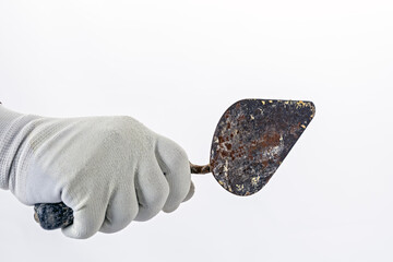 Hand in white rubber glove holds rusty metal trowel against plain background, suggesting focus on...