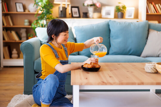 Woman pouring fresh orange juice while having breakfast at home