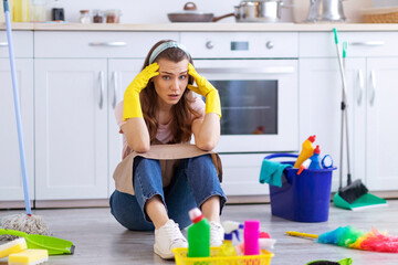 I need break. Exhausted housewife or maid sitting on floor at kitchen among cleaning supplies,...
