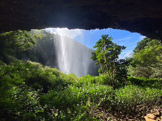 Blick aus der Höhle hinter einem Wasserfall auf tropische grüne Natur