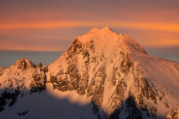 Aerial view of a majestic, snow-dusted peak bathed in the warm glow of the setting sun, casting long shadows across its craggy face, VysokÃ© Tatry, PreÅ¡ov Region, Slovakia.