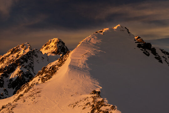 Fototapeta Aerial view of snow-capped peaks bask in the warm glow of the setting sun, creating a stunning contrast against the dark sky, VysokÃ© Tatry, PreÅ¡ov Region, Slovakia.