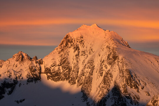 Aerial view of a majestic, snow-dusted peak bathed in the warm glow of the setting sun, casting long shadows across its craggy face, VysokÃ© Tatry, PreÅ¡ov Region, Slovakia.