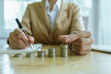 A hand places coins into a growing stack, symbolizing saving, investment, financial planning,...