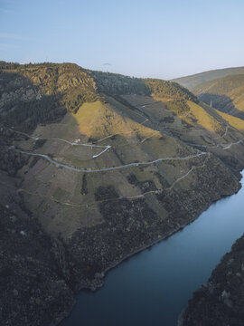Aerial view of the dramatic Sil River carves through rugged, terraced hills under a soft sky, Ribeira Sacra, Lugo, Spain.