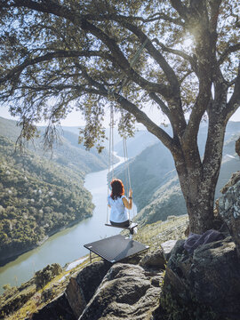 Aerial view of a person on a swing overlooking the Sil River canyon, a majestic body of water winding through verdant hills, Ribeira Sacra, Lugo, Spain.