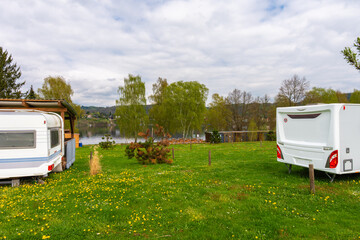 Vintage camper trailers parked by a quiet lakeside camping area in spring. Green grass, wildflowers, wooden shelter and peaceful outdoor travel lifestyle. No people, copy space
