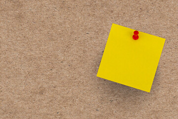 A blank yellow sticky note pinned to a brown cork notice board for an office reminder message