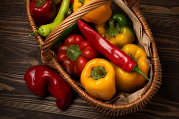 Colorful mix of sweet and hot peppers in a wicker basket on a dark wooden background. Fresh organic vegetables, perfect for healthy cooking and farm-to-table concepts