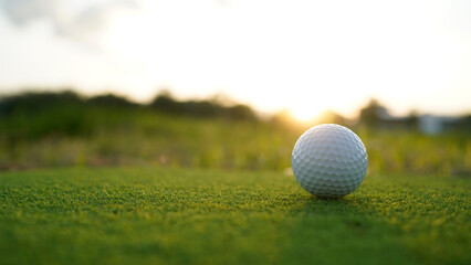 Golf ball on green grass in the evening golf course with sunshine background.
