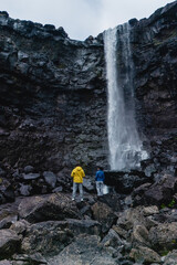 Visitors stand in awe at a stunning Fossa waterfall cascading down rocky cliffs in the Faroe Islands. The lush greenery and unique geological formations create a breathtaking backdrop.
