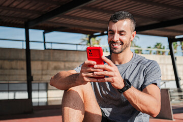 Cheerful man engaging with a fitness application on his smartphone during a break from workout activities, showcasing the connection between technology and fitness in an active lifestyle.