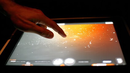 Close-up of a hand touching a glowing interactive tablet screen with data visualization