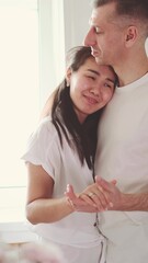Romantic married couple dancing at home near the window against a background of flowers