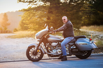 Stylish middle-aged man in a leather jacket sits confidently on a large cruiser motorcycle at...