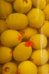 A close-up view reveals numerous green olives, some stuffed with red pimiento, packed tightly in a jar