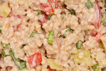 A close-up, top-down view captures the rich texture and vibrant colors of a barley salad, featuring diced peppers, tomatoes, and green onions mixed in a creamy dressing