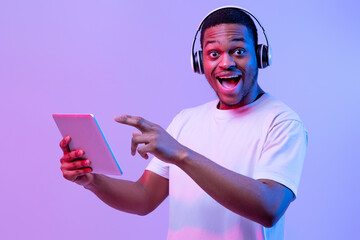 Check This App. Excited Black Man In Wireless Headphones Pointing At Digital Tablet While Browsing...
