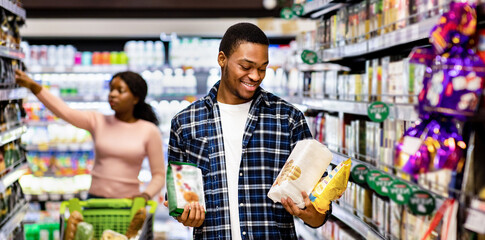 Black man and his girlfriend shopping for groceries, making selection of healthy food at mall, copy...