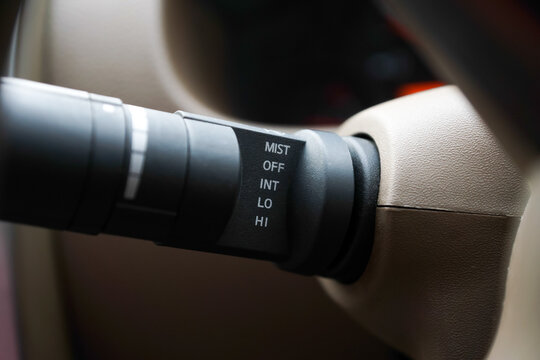Close-up of a car's windshield wiper control lever attached to the steering column, showing settings for mist, off, intermittent, low, and high speed. Automotive interior detail.