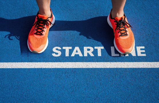 Feet wearing bright orange sneakers stand at start line of blue running track. Image captures moment of new beginnings, motivation, start of challenging journey. Dynamic composition readiness for