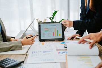 Business meeting with three professionals discussing strategy and collaboration while using laptops in a modern office setting.