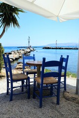 Traditional Greek taverna chairs and round table under a white umbrella facing the tranquil sea and...