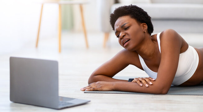 African American Fitness Beginner Lady Exercising At Laptop Exhausted After Online Workout Lying On Floor At Home. Difficulties Of Sporty Lifestyle And Weight Loss Burnout Concept - Powered by Adobe