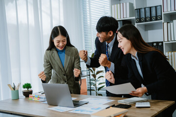 A group of three business men and women are having a meeting at a conference table. The woman is excited and her team members congratulate and encourage her.