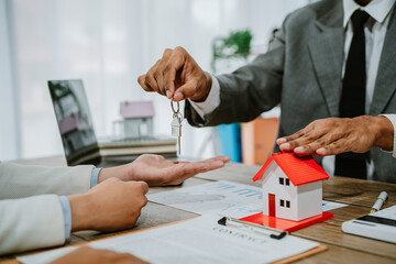 Smiling female realtor agent giving keys to apartment buyer. Homeowner receiving their new house...