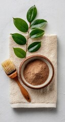 Natural face mask powder in a bowl, beside a brush and leaves on a towel