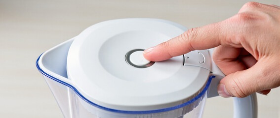 Finger Pressing Reset Button on Water Filter Pitcher Lid Close Up