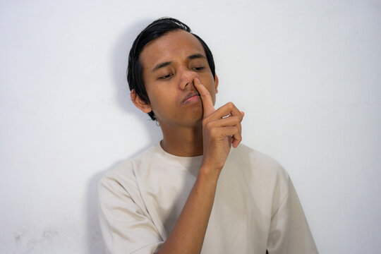 A young Asian man picking his nose with his finger, with a contemplative expression on his face.