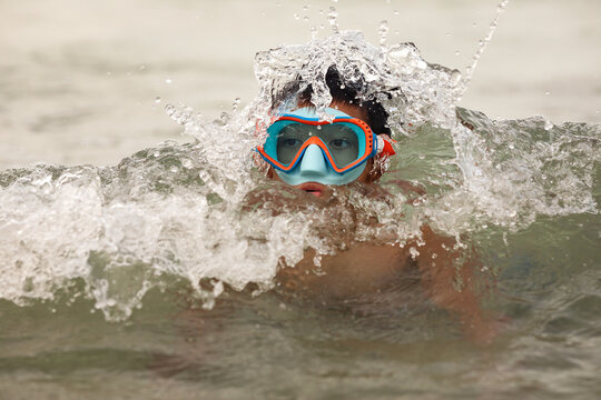 Child boy in big  goggles having fun playing in water with waves