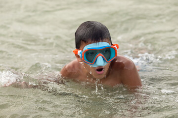 Child boy in goggles swimming in water at summer vacation