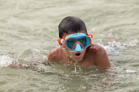 Child boy in goggles swimming in water at summer vacation