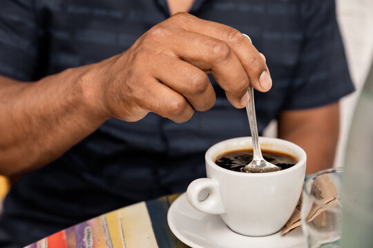 Man stirs sugar in hot black coffee in the morning at the cafe