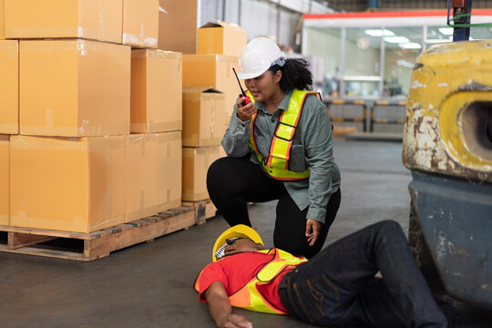 Female worker calling for help via walkie-talkie after a male colleague's accident in a warehouse. Represents workplace safety, emergency response, and industrial hazards