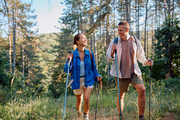 Couple walking through a lush forest, using trekking poles, enjoying the hike together and...