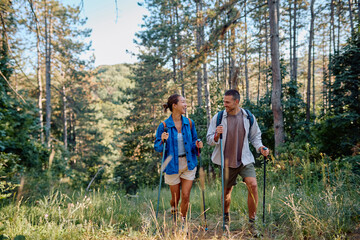 Happy couple hiking in the woods using trekking poles, enjoying the fresh air and stunning views