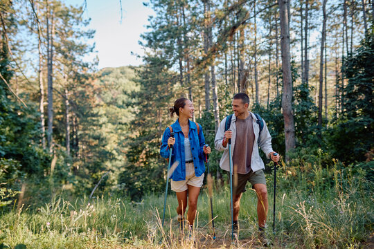 Happy couple hiking in the woods using trekking poles, enjoying the fresh air and stunning views - Powered by Adobe