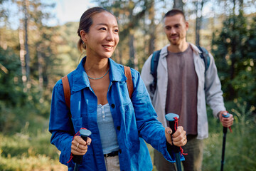 Happy couple walking in the forest using trekking poles and backpacks, enjoying a summer day in the...