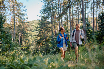 Couple of hikers with backpacks walking in a forest path and talking, enjoying a summer vacation day in the nature