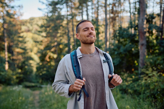 Young male hiker breathing fresh air and enjoying the peaceful nature during trekking in the forest - Powered by Adobe
